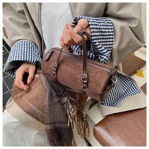 Detail of a dark brown cylindrical handbag in faux suede with leather straps and silver hardware