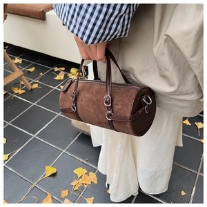 Detail of a brown cylindrical bucket bag featuring suede texture and leather straps
