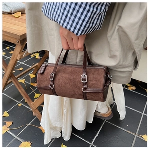 Detail of dark brown cylindrical handbag with suede texture and metal buckle accents