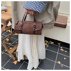 Close-up of brown suede cylinder bag with leather handles and silver metal buckles
