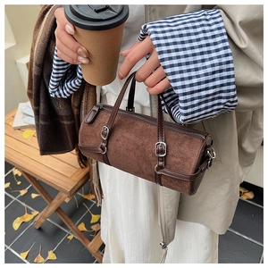 Close-up of brown barrel bag with leather buckle details and silver zipper hardware