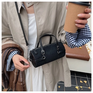 Detail of small black cylinder bag with matte texture and silver hardware in urban setting