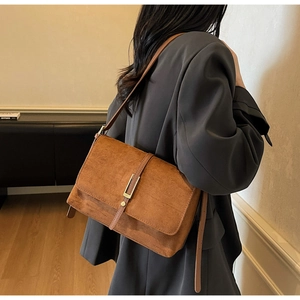 Detail of a brown matte suede shoulder bag with a metal buckle on a fashion model