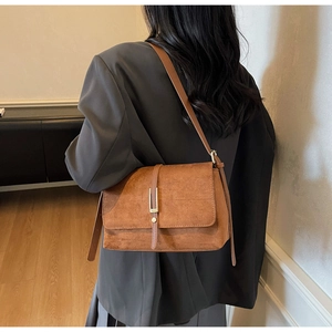 Detail of a brown suede shoulder bag with rectangular flap and minimalist metal buckle