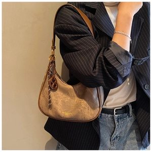 Détail du sac demi-lune en daim marron rétro avec pompon décoratif et logo doré
