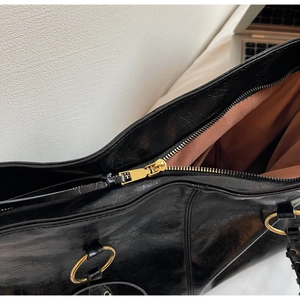 Detail einer schwarzen Lackleder-Tasche mit goldenem Reißverschluss und Beschlägen