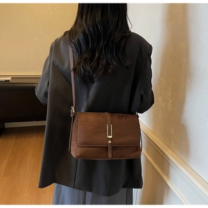 Detailed back view of a brown suede crossbody bag with gold buckle on a model in a suit