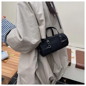 Minimalist black cylinder shoulder bag with silver hardware worn by a model in a modern room