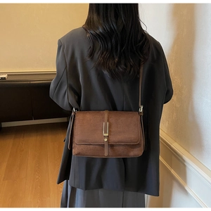 Detail of vintage brown suede shoulder bag featuring a sleek gold metal buckle and flap