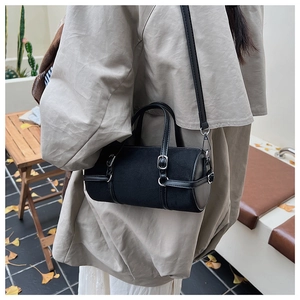 Detail of black cylindrical bag with matte finish and silver buckles on beige coat