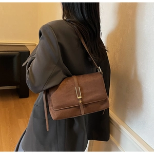 Brown suede shoulder bag with gold metal buckle detail on a charcoal grey blazer