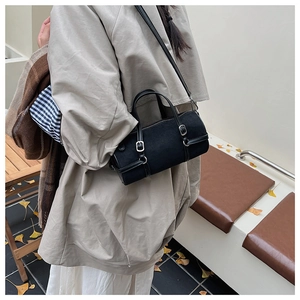 Close-up of black cylinder shoulder bag with leather straps and silver buckle detail