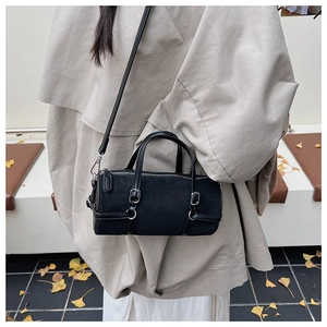 Detail of a black cylindrical shoulder bag with silver buckles on a beige trench coat