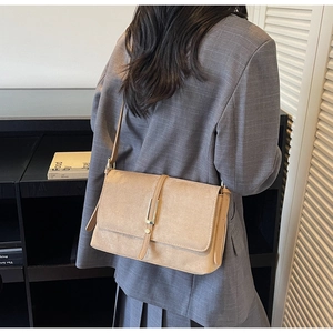Detail of warm khaki suede crossbody bag with gold buckle and adjustable strap