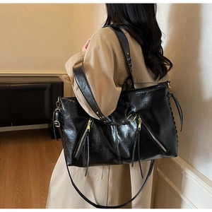 Detailansicht einer schwarzen Oversized-Tasche mit Metall-Reißverschlüssen und Web-Schultergurt