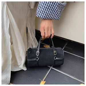 Detail of a black suede barrel bag with leather strap and silver buckle in a street style