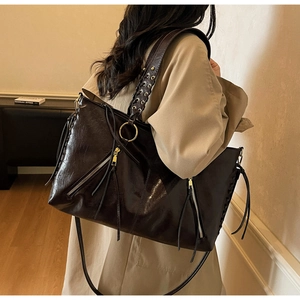 Detailaufnahme der braunen Vintage-Tote-Bag mit Webdetails und Quaste auf einem hellen Mantel