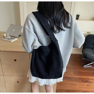 Détail d'un grand sac cabas en toile noire avec bandoulière large dans un intérieur