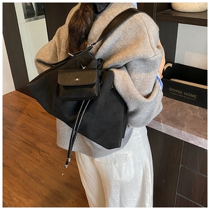 Detail of a large black canvas tote bag with a small leather pouch on a casual shoulder strap