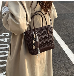 Detail of dark brown pleated tote bag with woven texture and chocolate charm on street