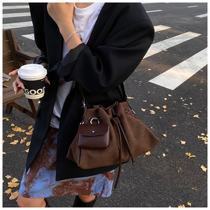 Brown suede bucket bag with drawstring closure and mini pouch on autumn leaf background