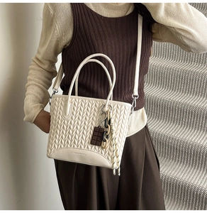 Detail of cream tote bag featuring textured quilting and embossed brand logo on the base