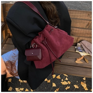 Detail of burgundy suede bucket bag with matching mini pouch on autumn bench background
