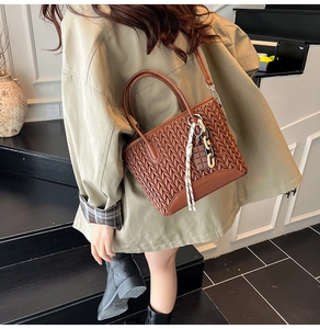 Detail of brown quilted bucket bag featuring round handles and a chocolate charm accessory