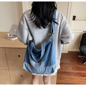 Détail d'un grand sac bandoulière en denim bleu avec poche avant sur mannequin