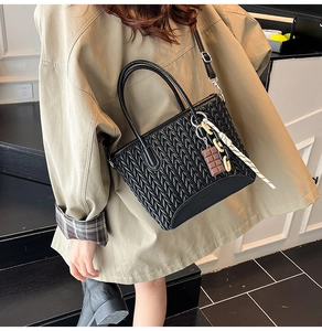 Detail of black quilted bucket bag with chocolate charm and woven rope on a trench coat
