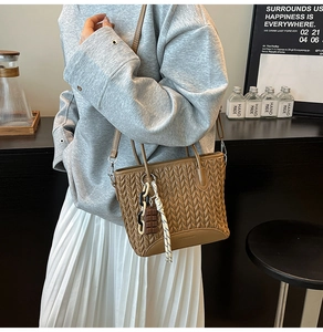 Detail of brown pleated bucket bag featuring chocolate pendant and woven rope strap