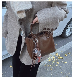 Borsa a secchiello in pelle cerata marrone scuro con ciondolo a orso su cappotto spigato