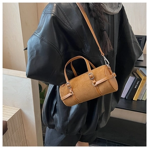 Model view of a brown suede cylinder bag with adjustable strap and silver buckle detail