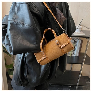 Brown suede cylinder bag shown with decorative straps and silver hardware on a model