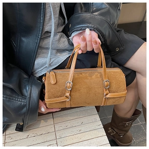Close-up of a brown suede cylinder bag featuring stylish strap details and silver hardware