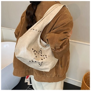 Detail view of cream hobo bag with star rivet pattern worn over a brown coat