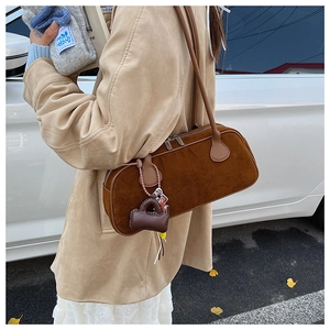 Detail of dark brown suede baguette bag with shoulder straps and matching mini bag charm