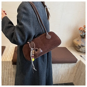 Detail of a large brown suede pillow bag with a long shoulder strap and charm