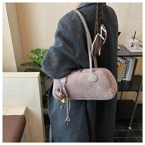 Detailed side view of tan suede baguette bag featuring heart charm on shoulder strap