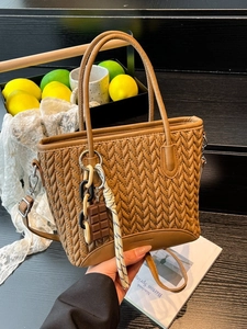 Quilted caramel brown crossbody bucket bag with woven texture on a minimalist black step