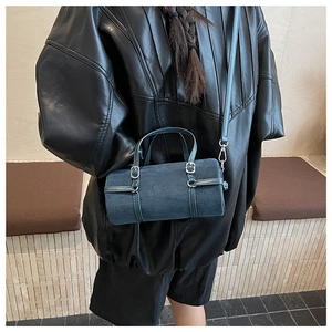 Detail view of navy blue cylinder handbag featuring decorative buckles and suede texture
