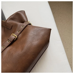 Close-up of brown leather tote bag detail with vintage gold buckle and metal eyelets
