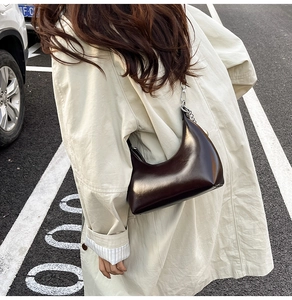 Close-up of a coffee brown patent leather crescent hobo bag worn with a beige trench coat