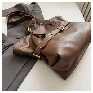 Close-up of vintage brown leather tote bag with decorative gold buckle on grey blazer