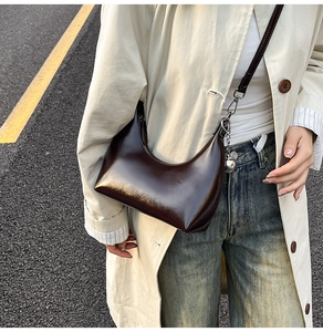 Detail of a dark brown glossy hobo bag with a silver sphere charm in a street style view