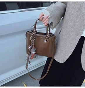 Dettaglio della borsa a secchiello vintage in pelle cerata marrone con ciondolo a orsetto