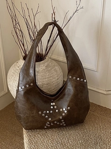 Vintage brown leather hobo bag with silver star rivets displayed in a cozy home setting