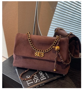 Detail of dark brown suede shoulder bag featuring a gold chain strap and textured lock