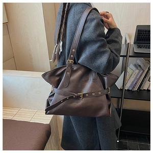 Detail of dark brown tote bag with metal buckle and soft pleated texture on shoulder