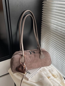 Retro tan suede baguette shoulder bag with slim straps and double zip on art book background